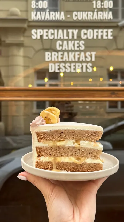 A slice of layered banana cake held in front of the café window